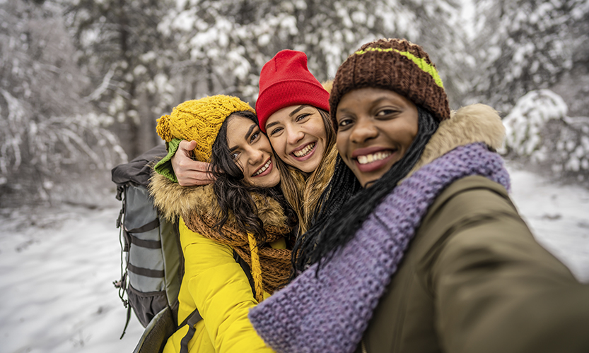 Talvisessa ulkokuvassa kolme nuorta iloista naista katsoo kameraan ja ottaa selfietä.