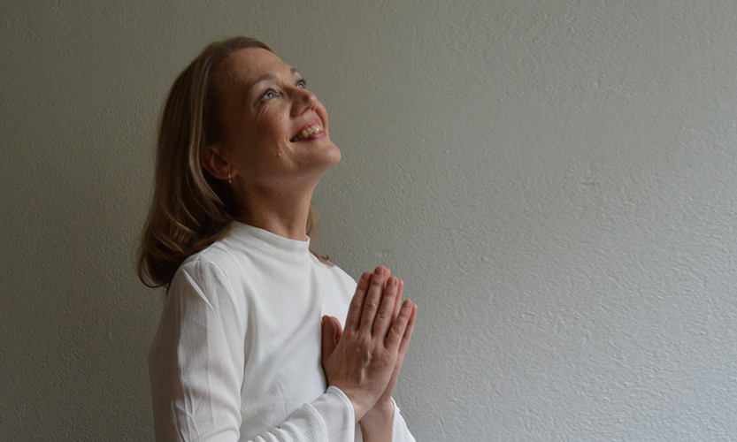 Kuvassa pitkätukkainen ja valkopaitainen nainen rukoilee ja katsoo ylöspäin.