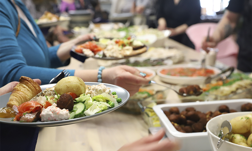 Kuvassa ihmisiä ottamassa ruokaa tarjoilupöydän äärellä.