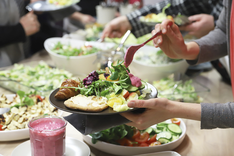 Kuvassa henkilö ottaa ruokaa noutopöydästä lautasellleen.