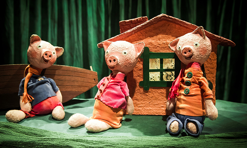 kuvassa on kolme pientä porsasnukkea ja niiden taustalla pieni mökki