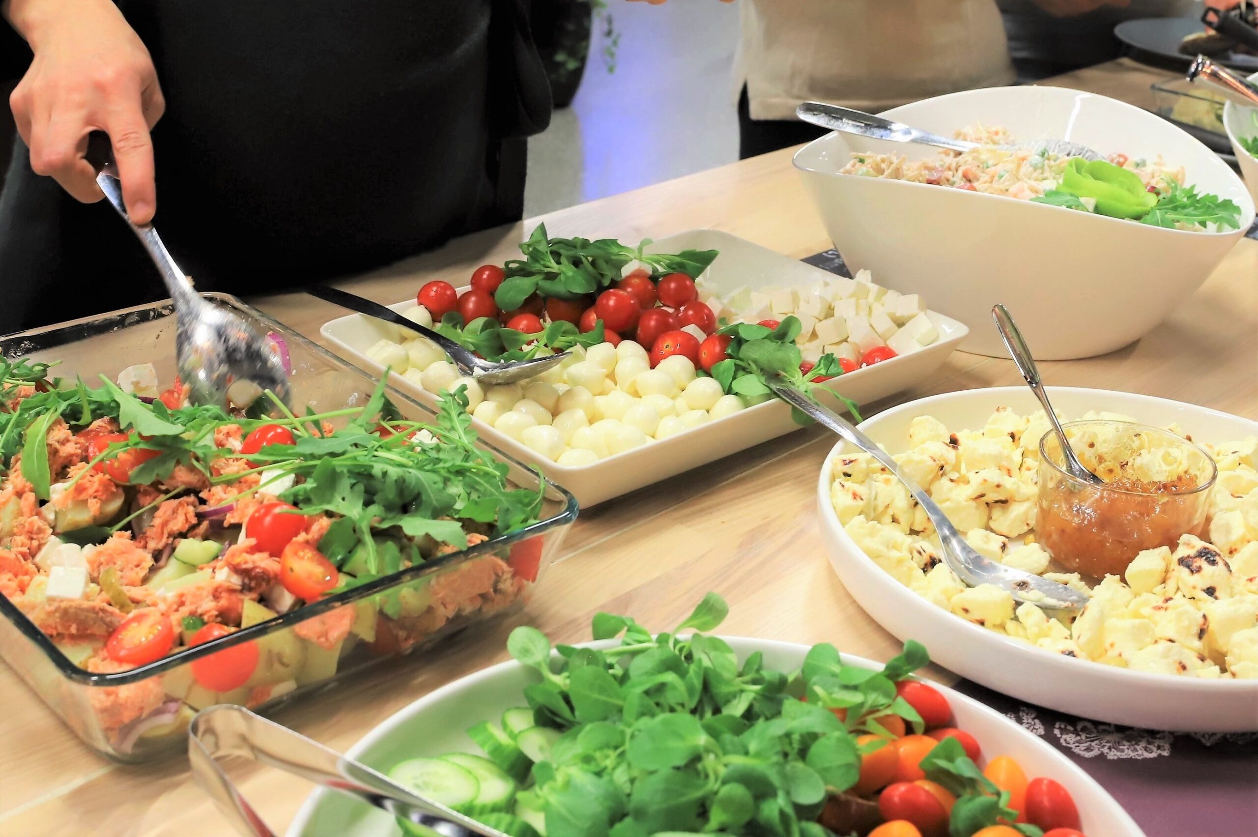 Tarjoiluvateja, joissa salaatteja ja juustokuutioita.