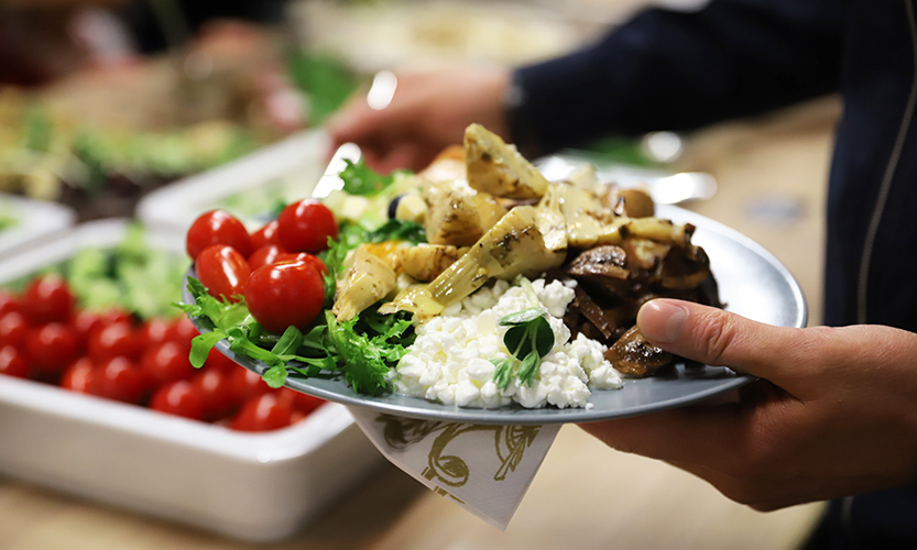 Henkilö pitää kädessään ruoalla täyttämäänsä lautasta. Taustalla näkyy brunssitarjoiluita.