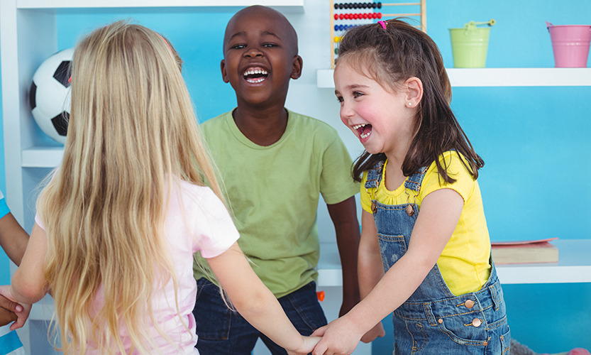 Kuvassa on iloisia, leikkiviä lapsia, jotka pitävät toisiaan kädestä kiinni.