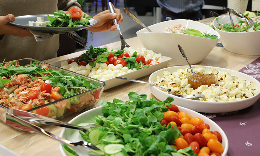 Tarjoilupöydälle on katettu monenlaisia värikkäitä kasviksia, salaatteja ja erilaisia juustoja.