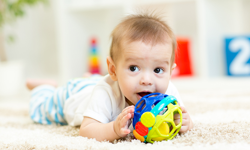 Söpö vauva makoilee pehmeällä matolla lastenhuoneessa lelua käsissään pitäen.